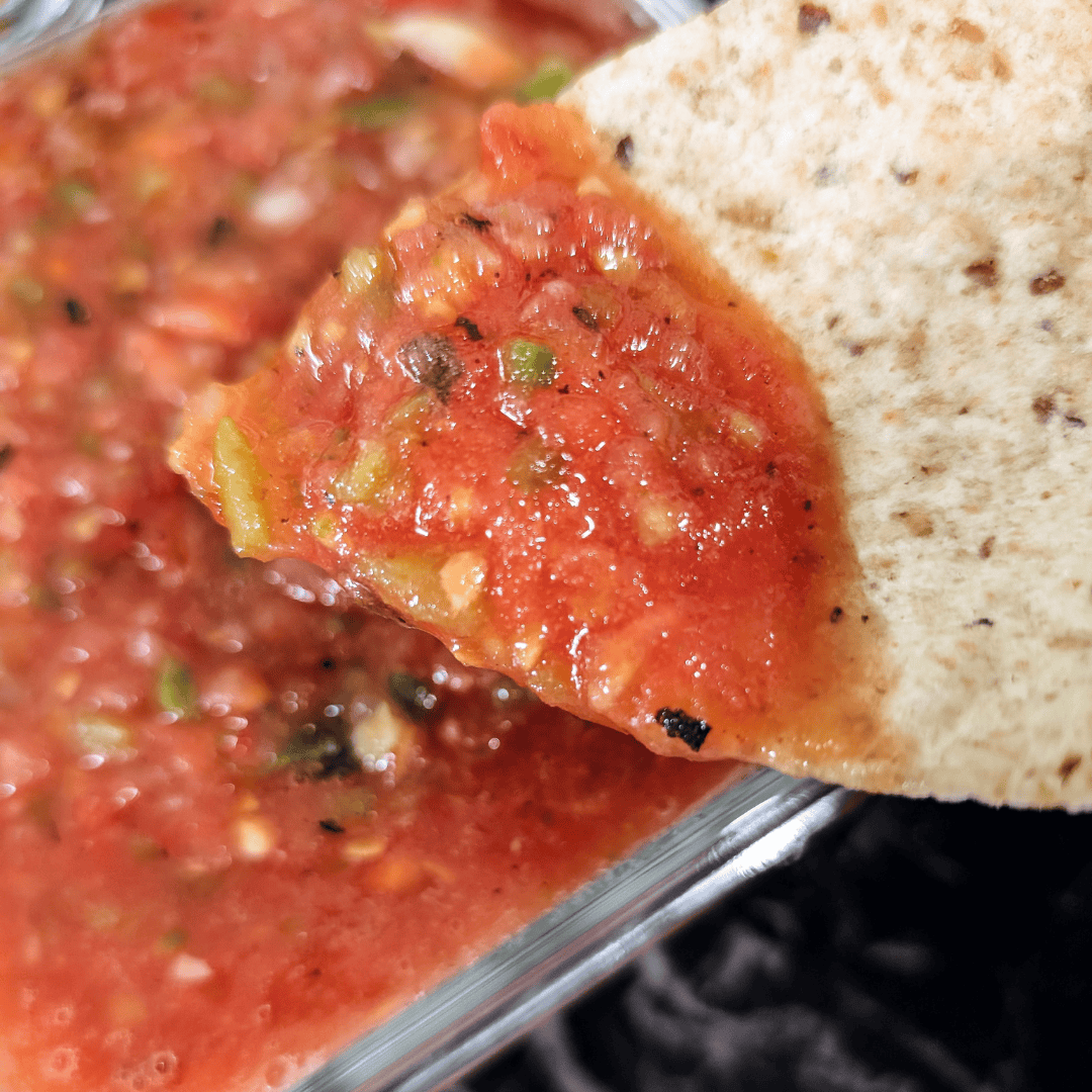 Close-up of roasted tomato salsa with cilantro and a tortilla chip.