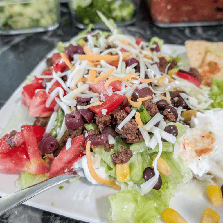 Fresh taco salad with ground beef, cheese, tomatoes, and lettuce on a white plate.