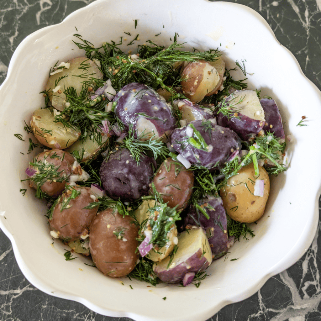 Colorful baby potatoes with dill and herbs in a white bowl.
