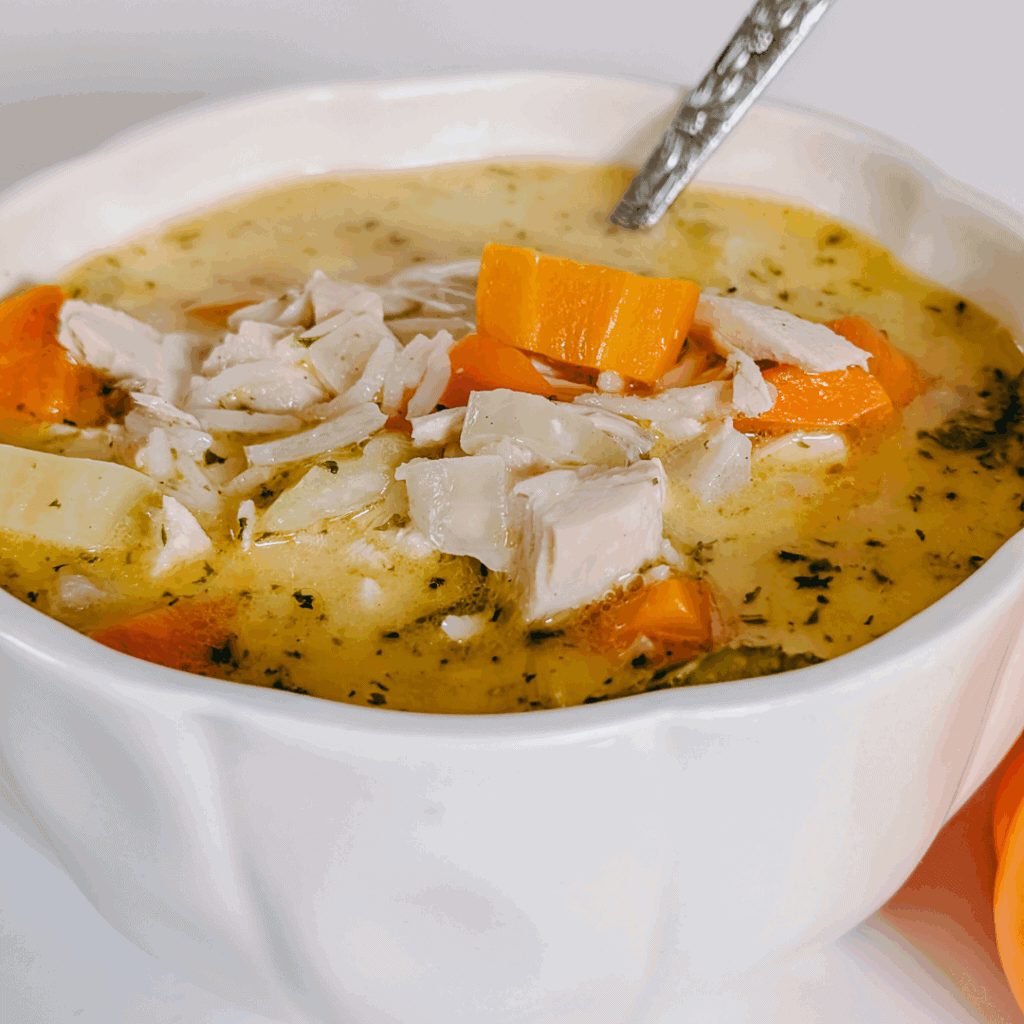 Creamy chicken vegetable soup in a white bowl with a spoon, fresh and comforting dish.