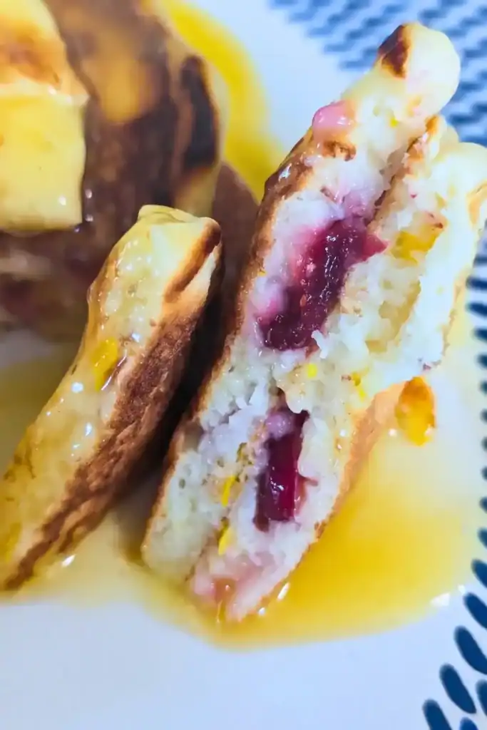 inside view of cut open cranberry orange pancakes in orange sauce on blue and white plate