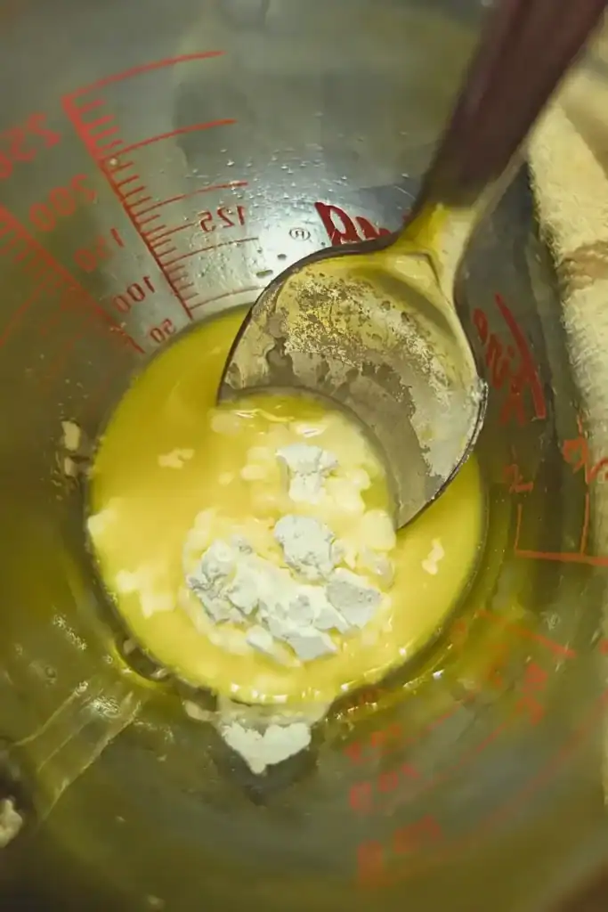 mixing cornstarch and orange juice in measuring cup with spoon