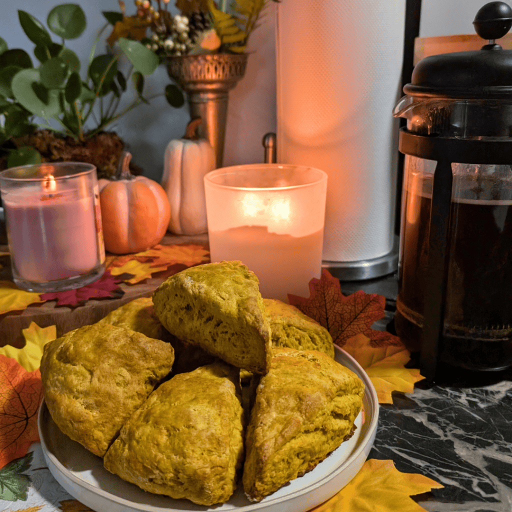 scones on plate in foreground candles lit behind for mood lighting a fall floral arrangement nearby and a bodum of fresh pressed coffee