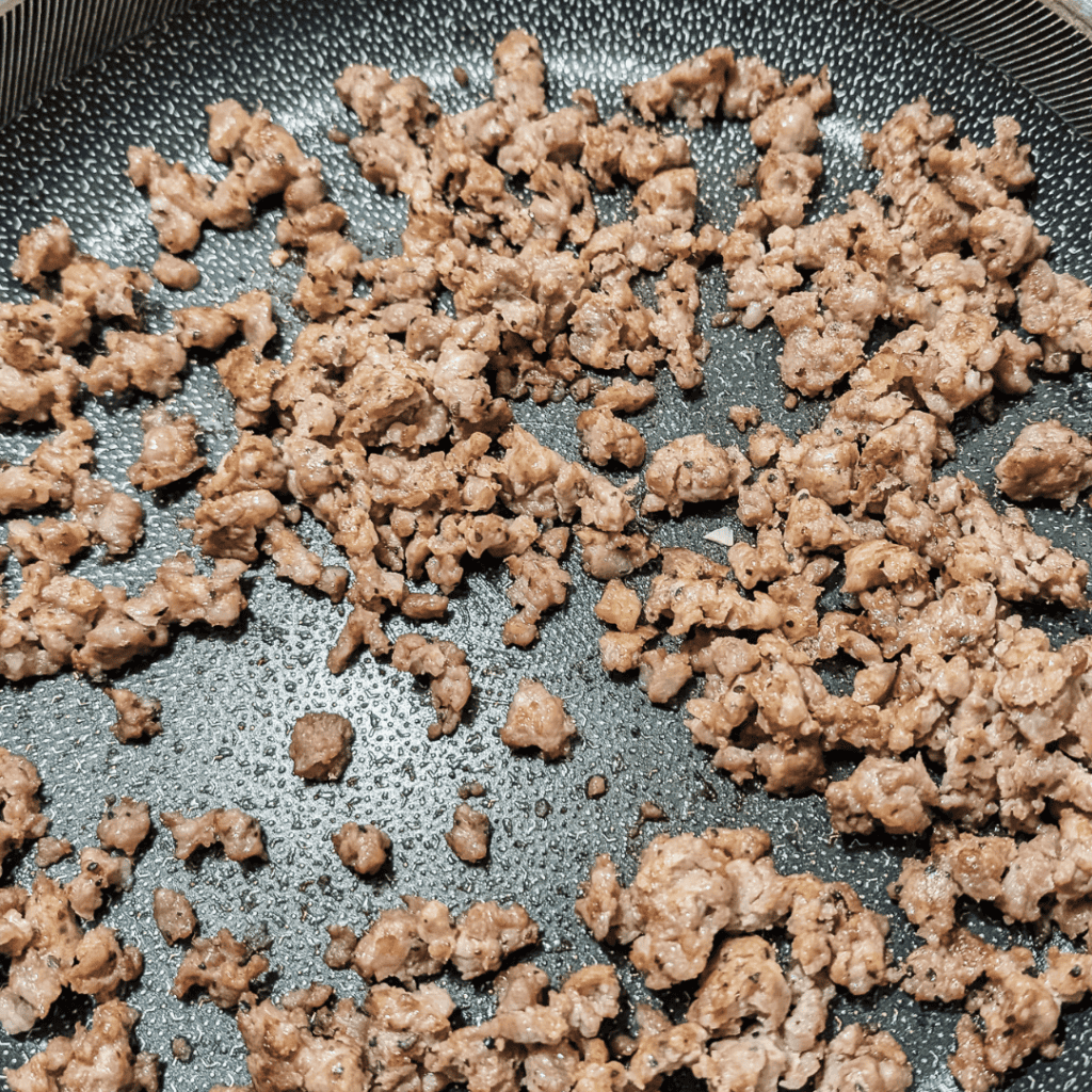 Cooked sausage crumbles in a skillet, ready for a spinach frittata.