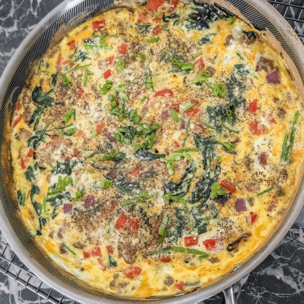Sausage and spinach frittata with fresh herbs in a skillet. Perfect for breakfast or brunch.