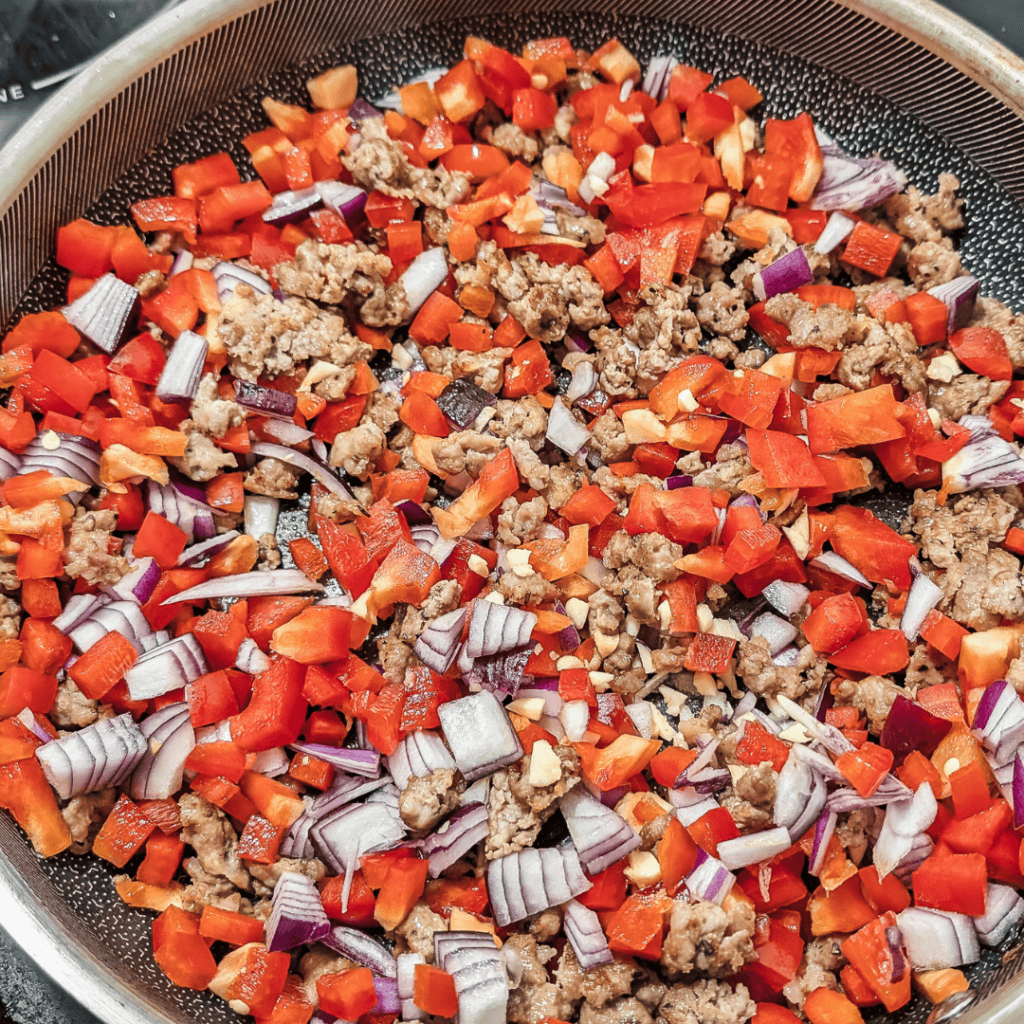 Cooked sausage, spinach, and red peppers in a skillet for a frittata.