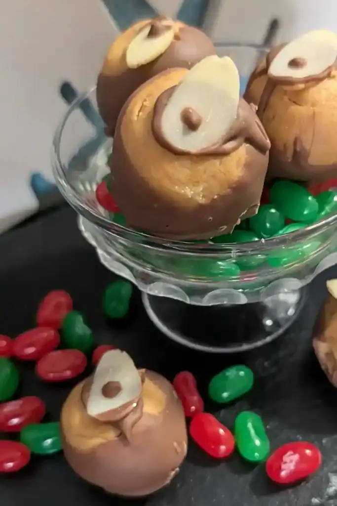 three buckeyes in a candy dish with red and green jelly beans and one sitting on tray with more beans below