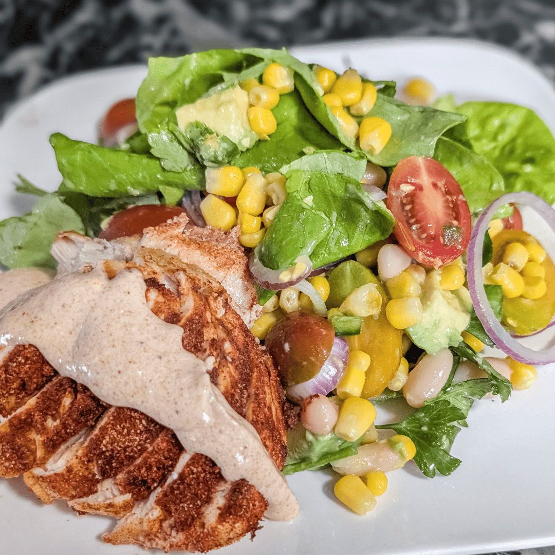 Fresh grilled chicken salad with corn, cherry tomatoes, and greens on a white plate.