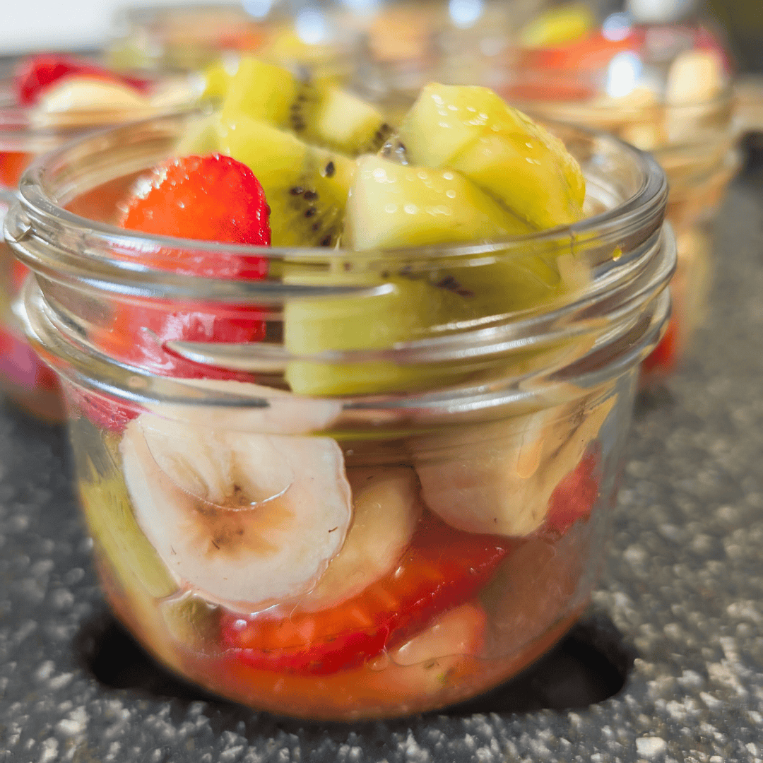 Fresh fruit salad in glass jar with strawberries, bananas, kiwi, and other mixed fruits, healthy homemade snack or dessert, vibrant colorful fruit mix.