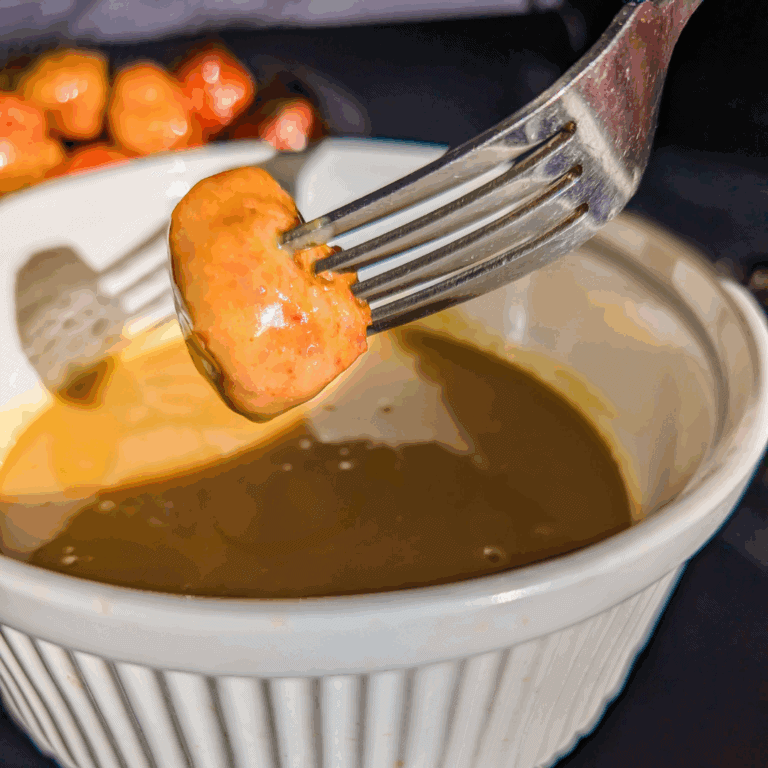 Juicy sausage being dipped in rich gravy in a white ramekin.