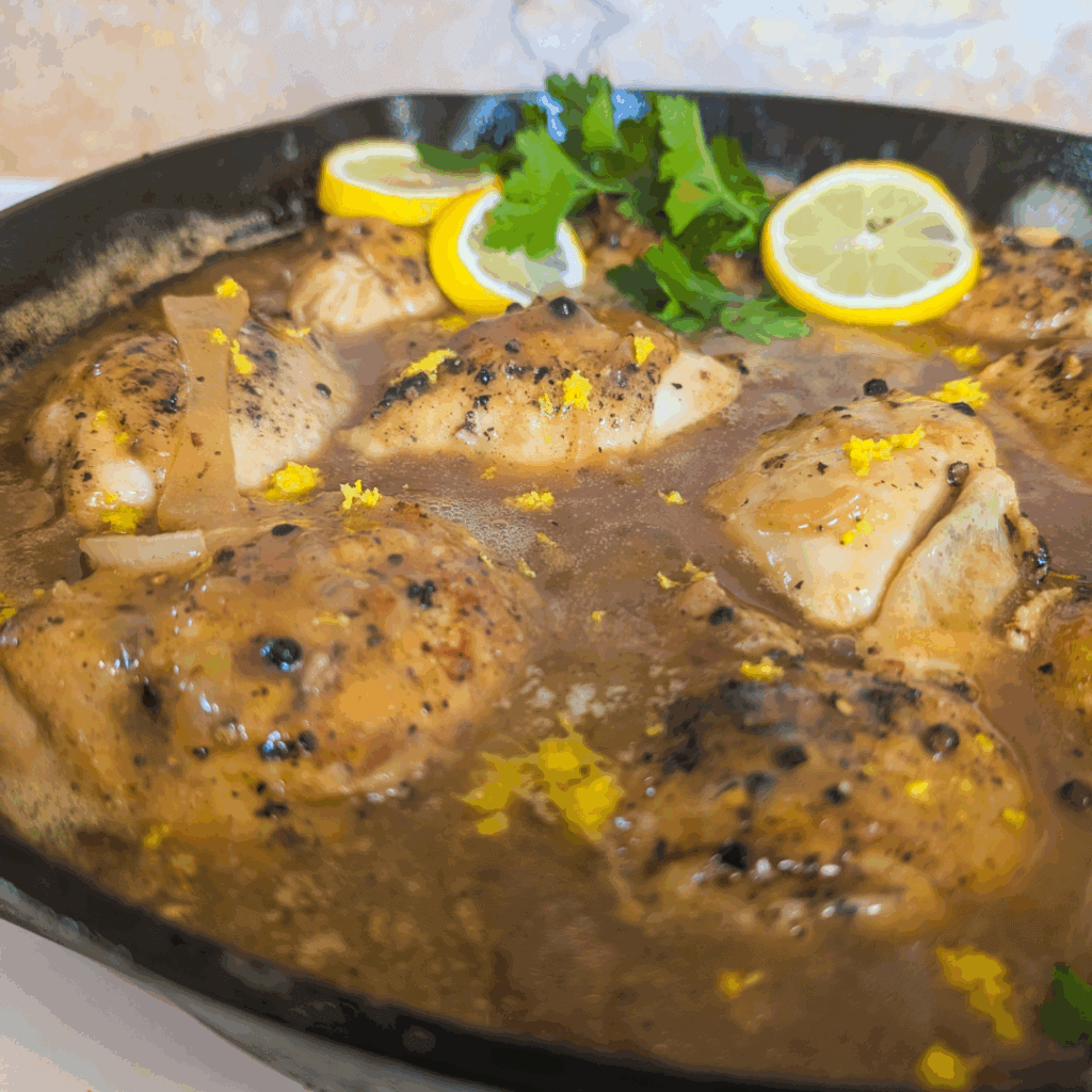Succulent chicken in lemon herb sauce, garnished with lemon slices and fresh cilantro, served in a skillet.