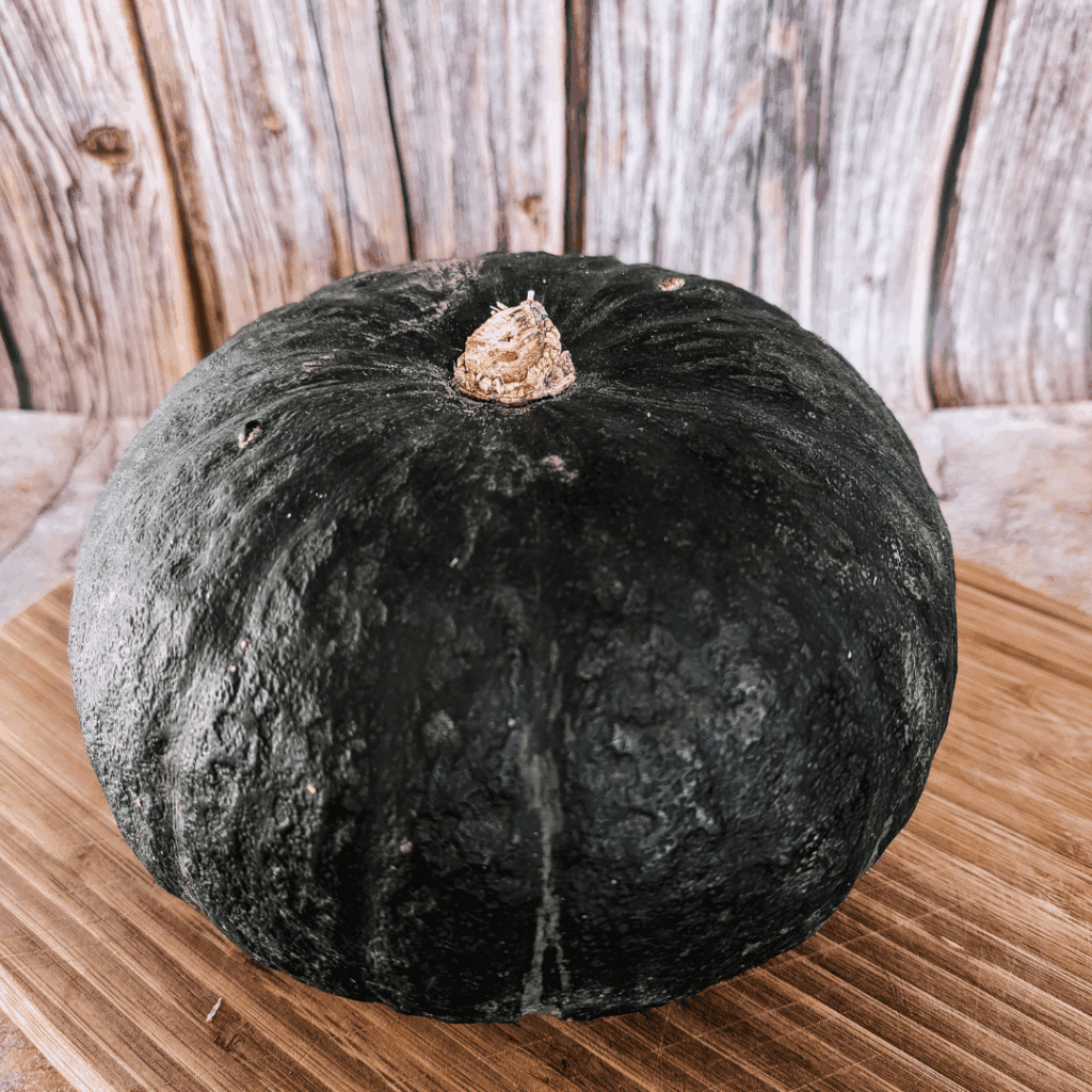 Black pumpkin on wooden cutting board, rustic kitchen background.