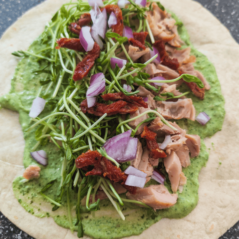 Delicious chicken wrap with greens, sun-dried tomatoes, and onion on a tortilla.