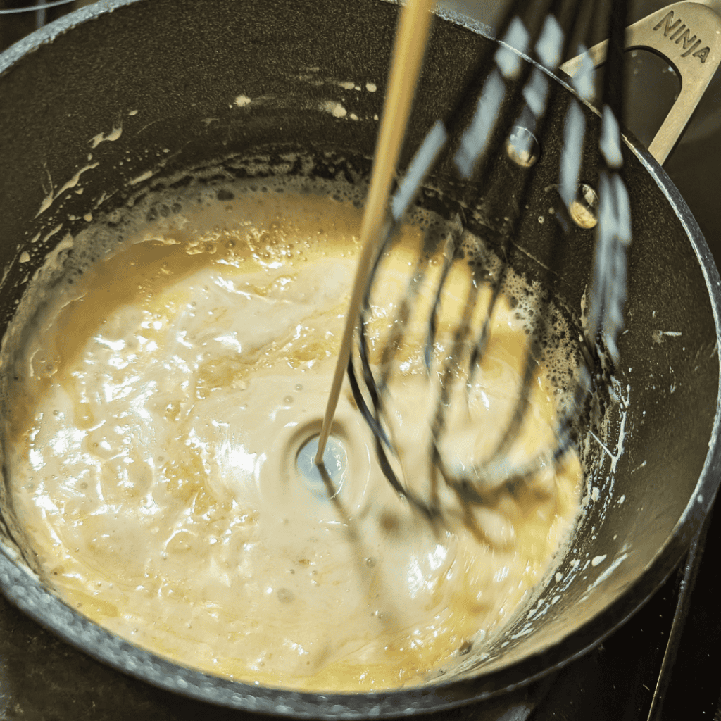 Cheddar cheese sauce being prepared in a saucepan with a whisk for burgers.