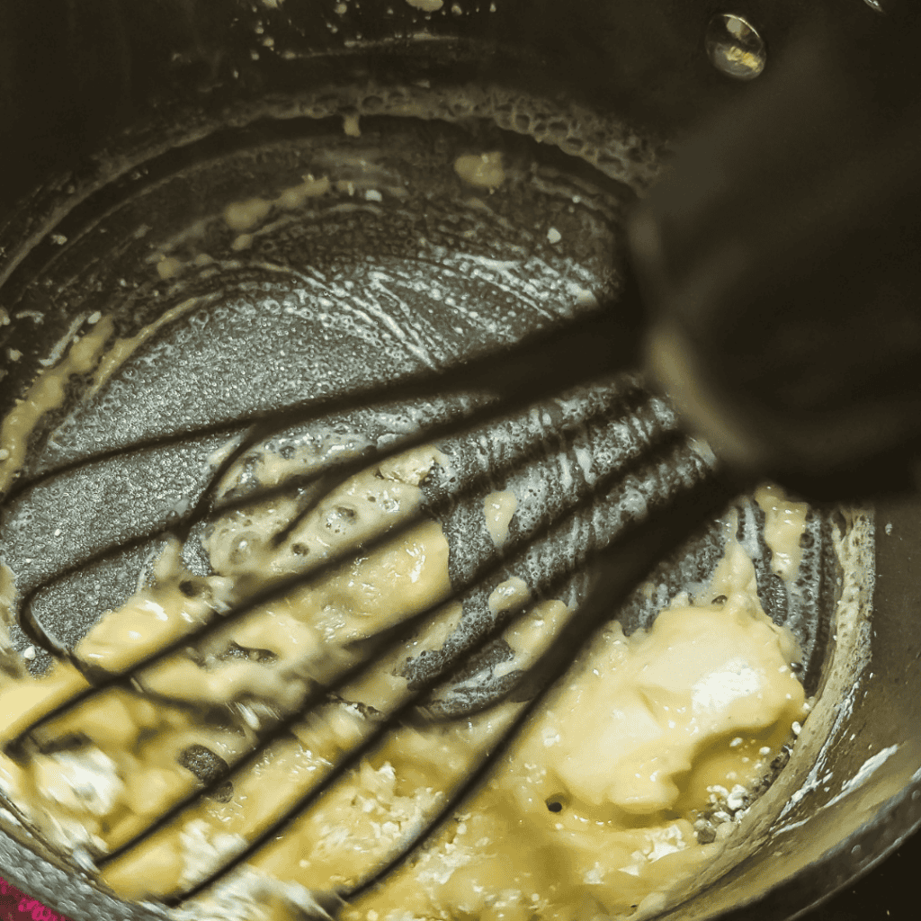 Creamy cheddar cheese sauce in a saucepan with a whisk.