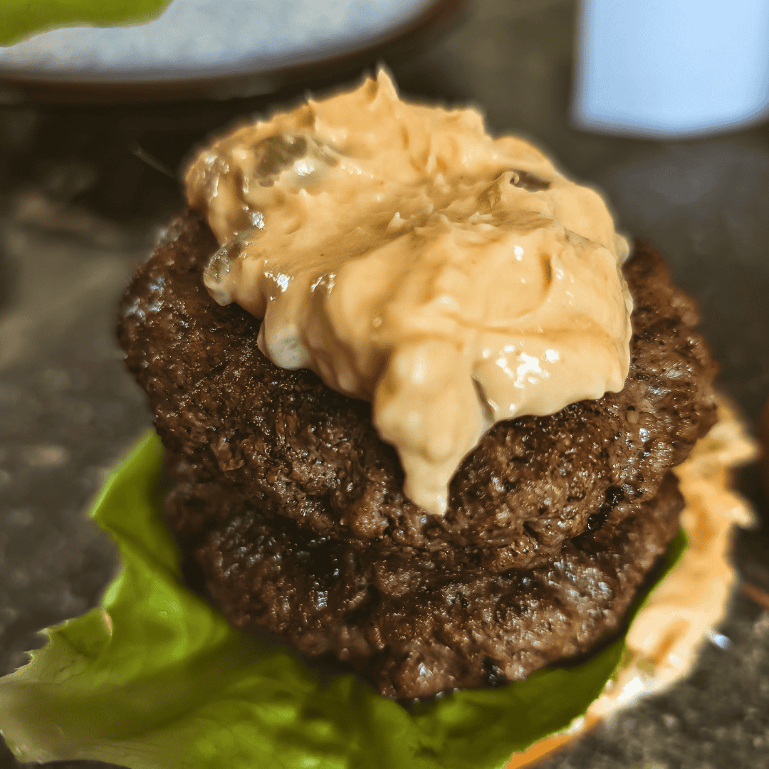 Juicy burger patty topped with creamy cheddar cheese sauce on lettuce.