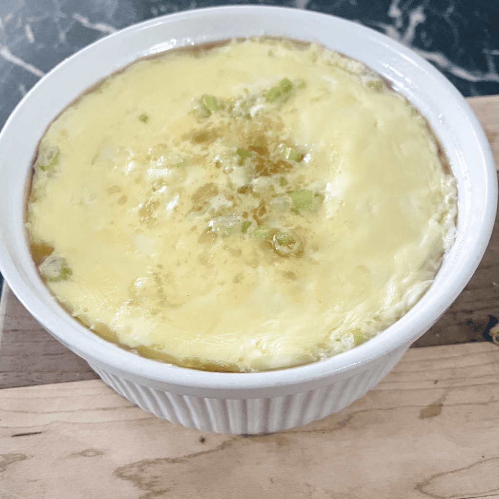 Egg drop soup with green onions in a white bowl.