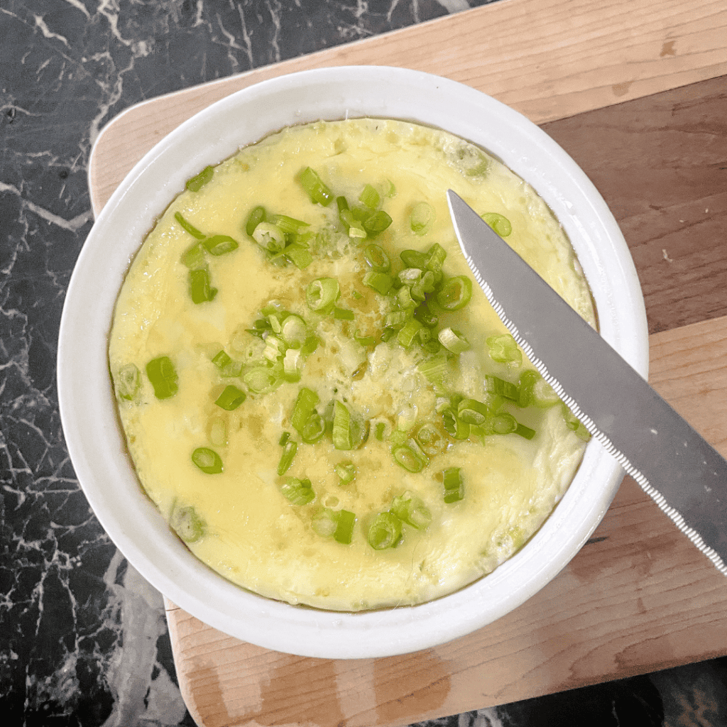 Fresh egg omelette topped with chopped green onions on a wooden cutting board.