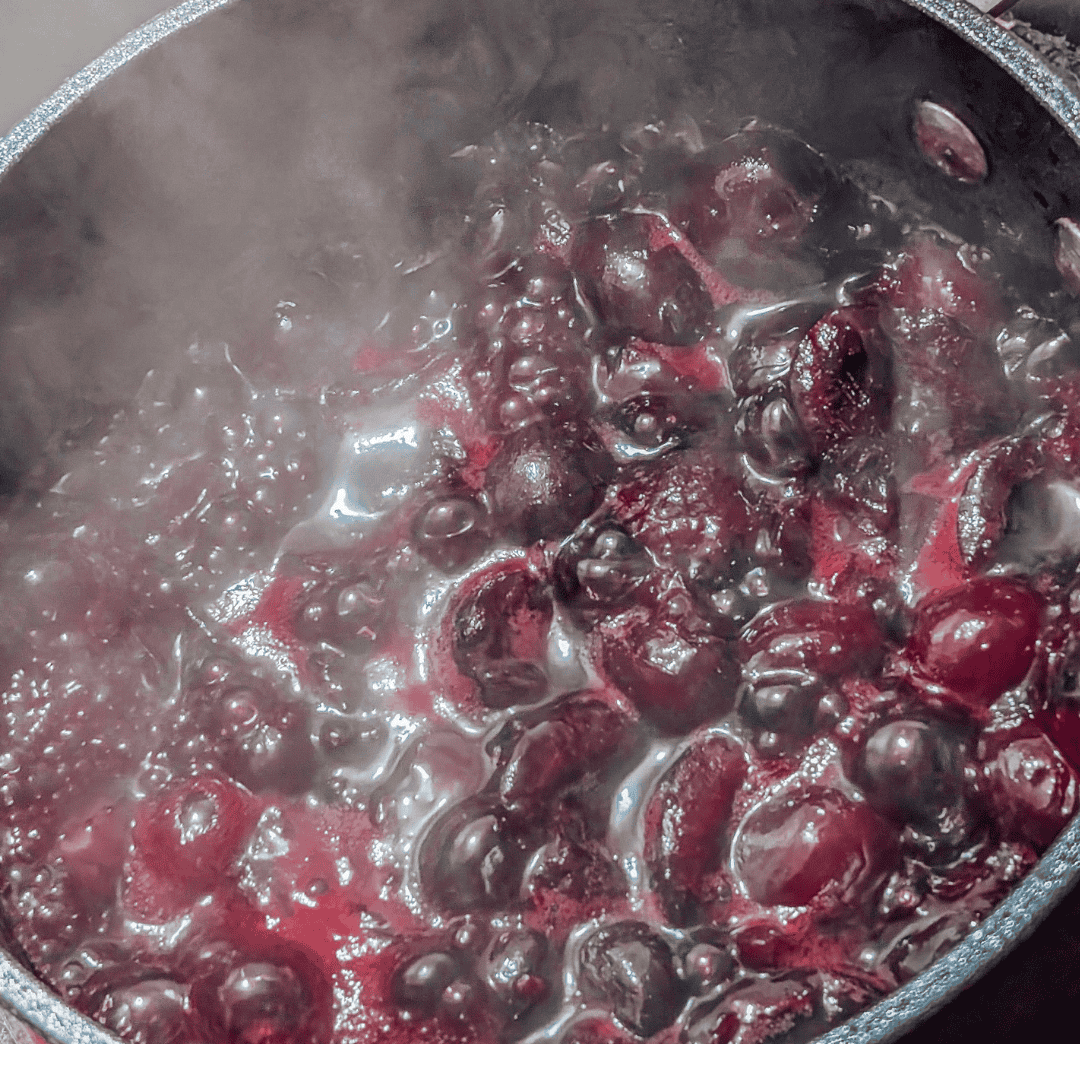 Boiling fresh cherries in a pot for homemade cherry jam or syrup.