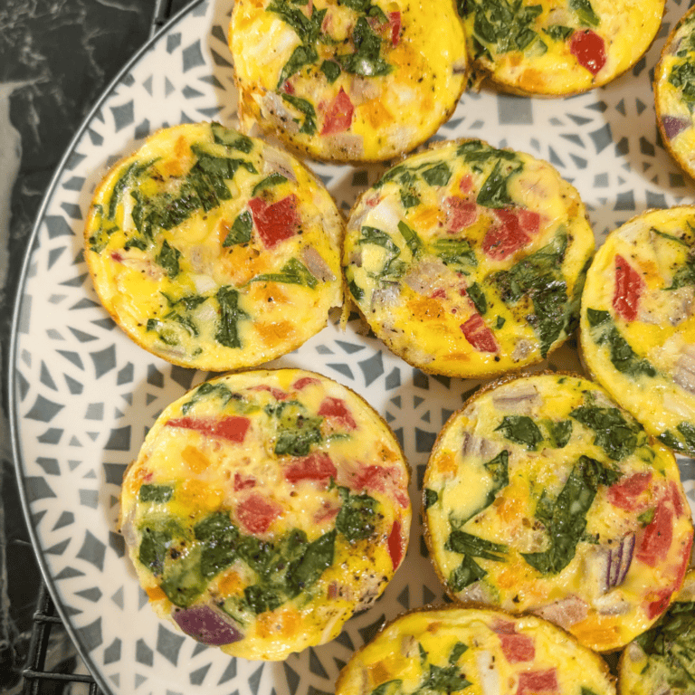 Delicious mini vegetable frittatas with colorful peppers and greens on a patterned plate.