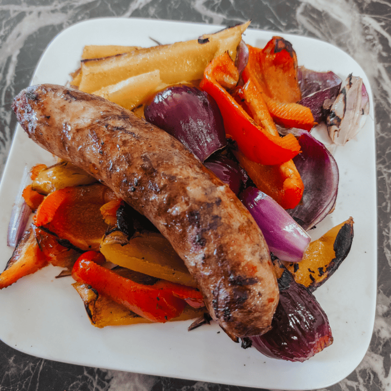 Juicy grilled sausage served with roasted bell peppers, onions, and potatoes on a white plate.