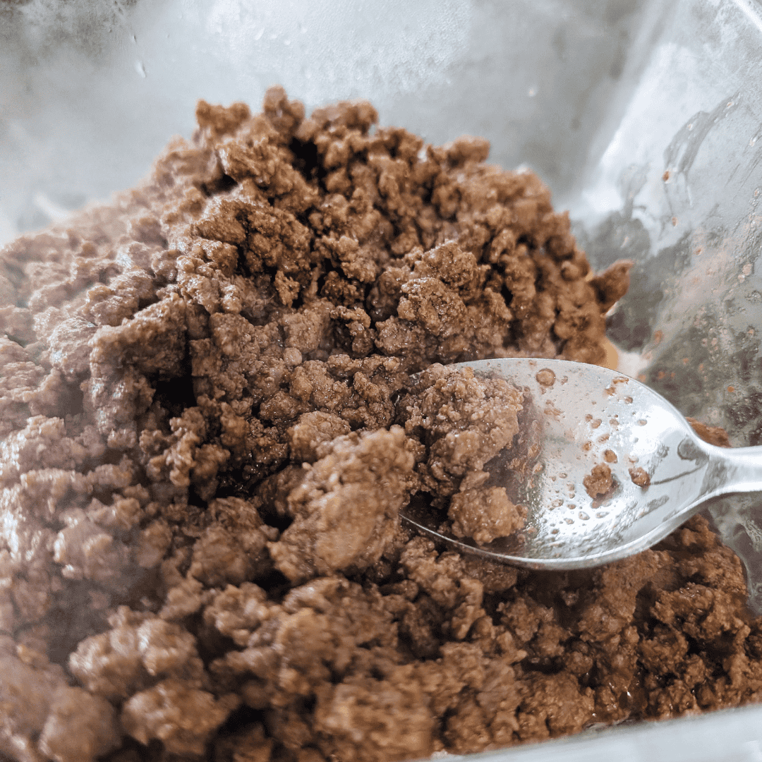 Ground beef for taco meat in a glass bowl with a spoon.
