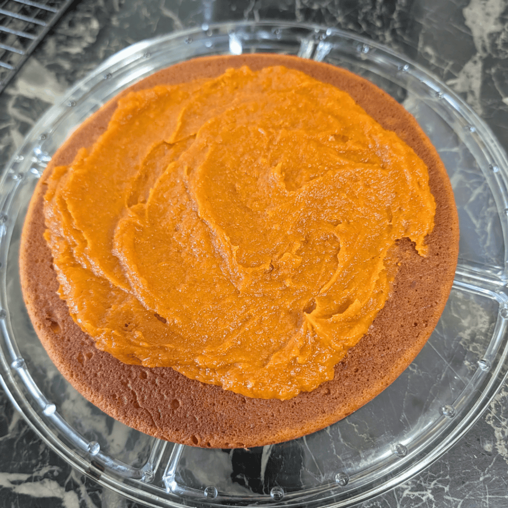 spreading pumpkin cake filling onto bottom of cake