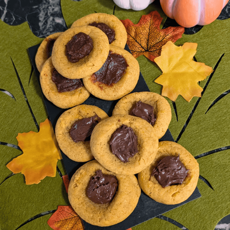 soft pumpkin thumbprint cookies with apple butter and nutella filling on black plate sitting on fall green leaf felt placement with fall leaves and mini pumpkins